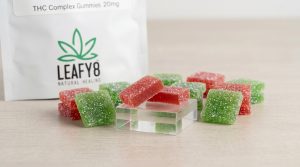 Clean macro product shot of Leafy8 THC Complex Gummies (20mg) in a local Florida dispensary setting, featuring naturally colored red and green square gummies dusted in sugar coating next to official Leafy8 Natural Healing product packaging on a light studio background.